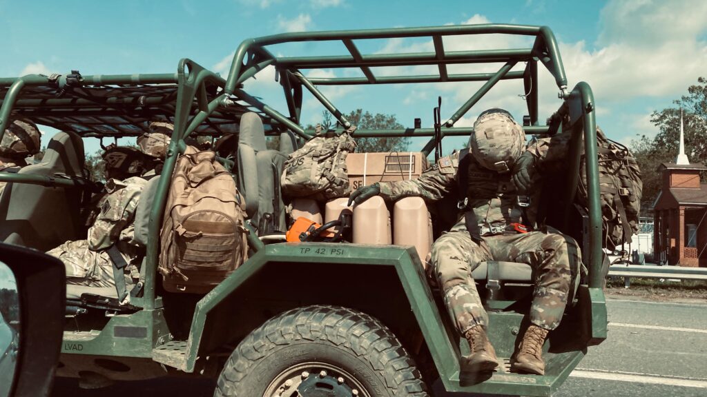 Photo of military vehicle and people in uniforms, with several looking exhausted.